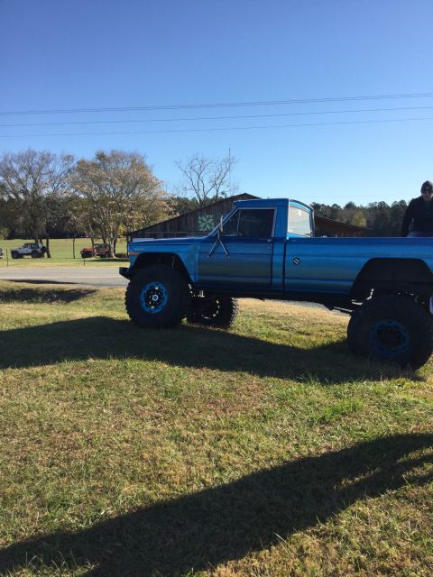 1979 Ford Bronco - A lifted, bright blue pickup truck with large off-road tires is parked on a grassy field under a clear blue sky. The truck has a single cab…