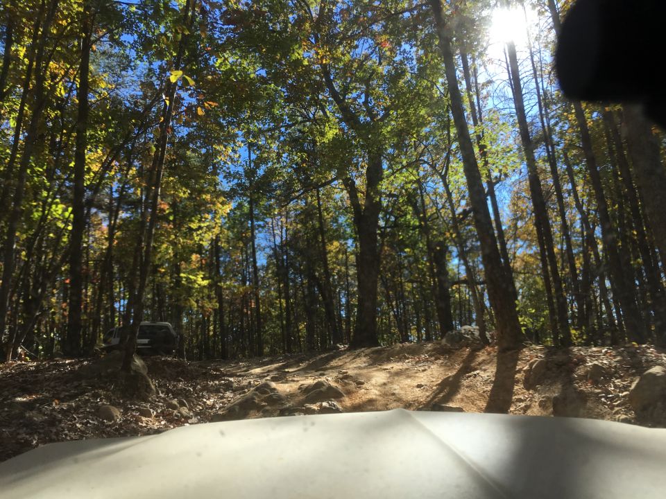 SUV parked on a rocky trail in a forest with sunlight filtering through autumn leaves.
