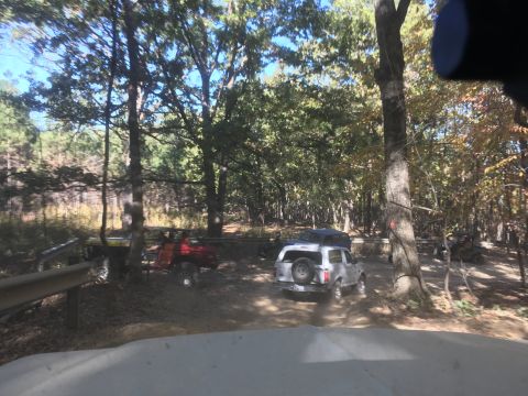 1979 Ford Bronco - A white Ford Bronco is driving on a dirt path through a wooded area with several other off-road vehicles visible. The Bronco has a spare ti…