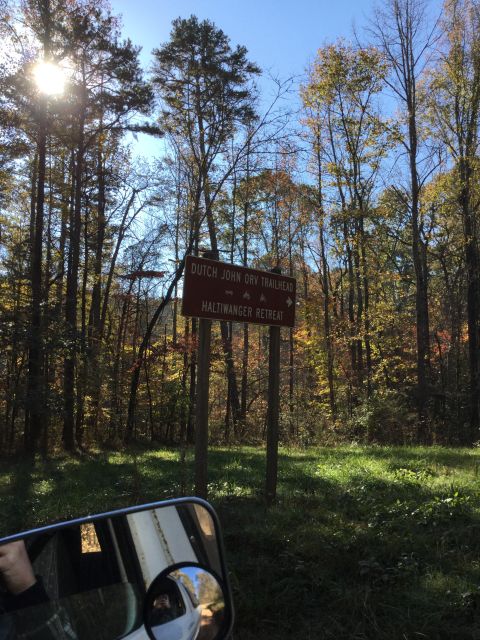 1979 Ford Bronco - A sign for Dutch John ORV Trailhead and Haltiwanger Retreat is visible in a wooded area with fall foliage. The reflection of a vehicle, lik…