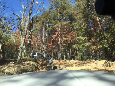 1979 Ford Bronco - A white SUV with a spare tire mounted on the rear is navigating a rocky, wooded trail during autumn. The vehicle is partially obscured by t…