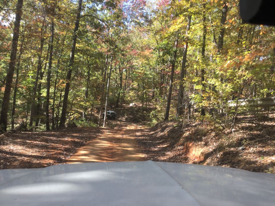 White SUV on a dirt road in a forest with autumn foliage.