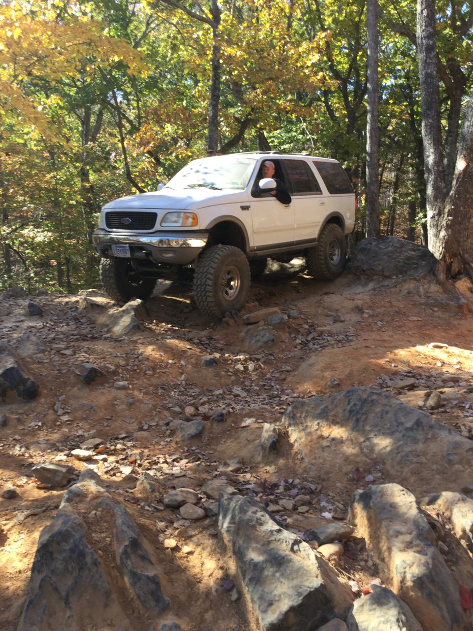 White Ford Expedition off-roading on a rocky trail with fall leaves.