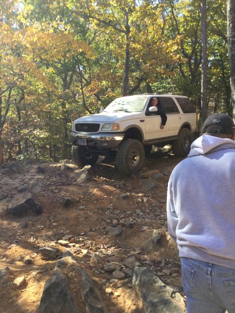 1979 Ford Bronco - A lifted white Ford Expedition with large tires navigates a rocky, wooded trail during autumn. A person is visible leaning out of the drive…