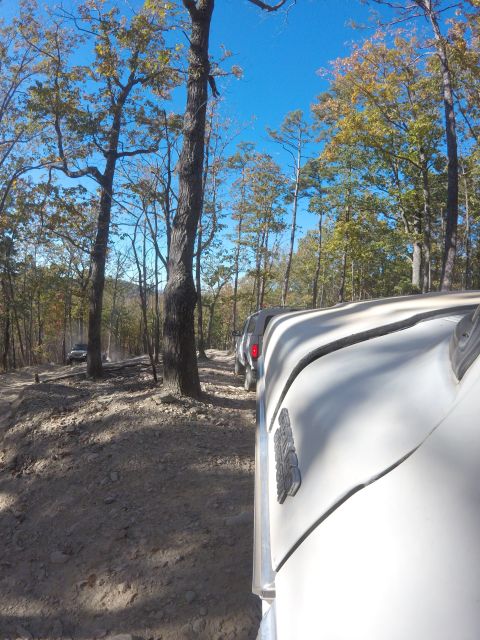 1979 Ford Bronco - A white vehicle is parked on a dirt road surrounded by trees with autumn foliage. Another vehicle is visible further down the road.