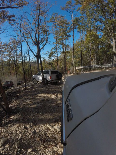 1979 Ford Bronco - A white Ford Bronco is parked on a rocky, wooded trail, with another red SUV in the distance. The photo is taken from the perspective of an…