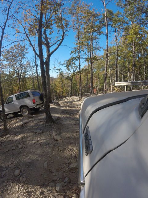 1979 Ford Bronco - A white Ford Bronco is parked on a rocky, wooded trail during the fall. Another vehicle is visible in the foreground, partially obscuring t…