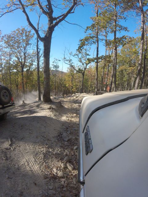 1979 Ford Bronco - A white vehicle drives on a dusty, rocky trail through a forest with autumn foliage. The side of the vehicle and a spare tire on another ve…