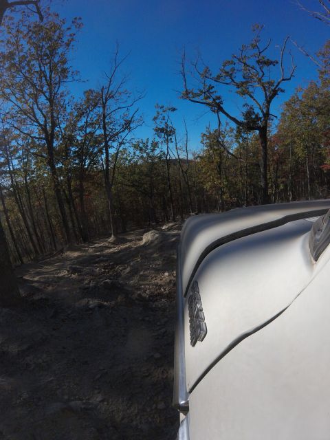 1979 Ford Bronco - The right side of a white 1979 Ford Bronco is visible as it drives on a rocky, wooded trail under a clear blue sky. The vehicle's fender an…