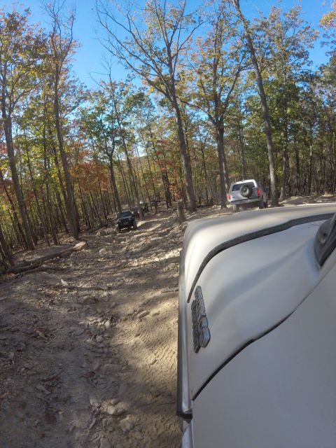 1979 Ford Bronco - A white Ford Bronco is seen from a low angle, driving on a rocky off-road trail through a forest with autumn foliage. Another black vehicle…