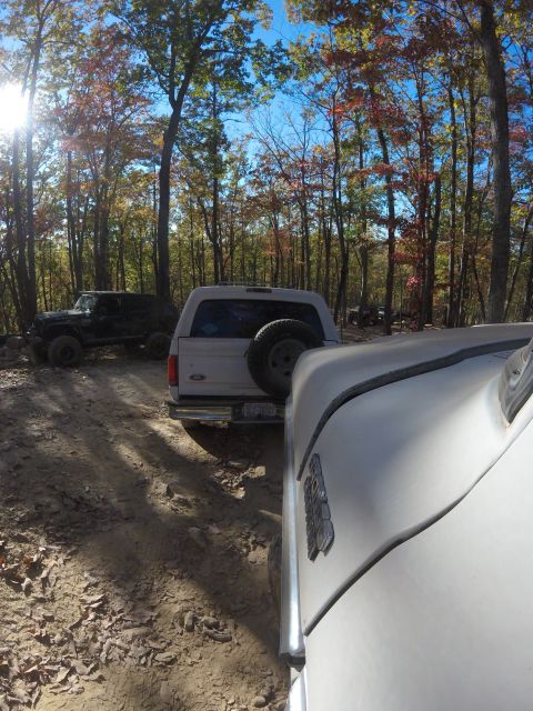 1979 Ford Bronco - A white Ford Bronco is parked on a dirt road in a forest with colorful autumn leaves. Another black SUV is visible behind it.