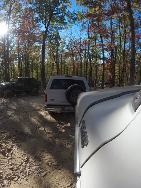 1979 Ford Bronco - A white Ford Bronco is parked on a dirt path surrounded by trees with autumn foliage. The front of another vehicle is visible in the foregr…