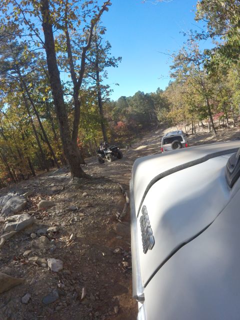 1979 Ford Bronco - A white Ford Bronco is seen from a low angle, driving on a dirt and rock trail through a wooded area with fall foliage. Another ATV is visi…