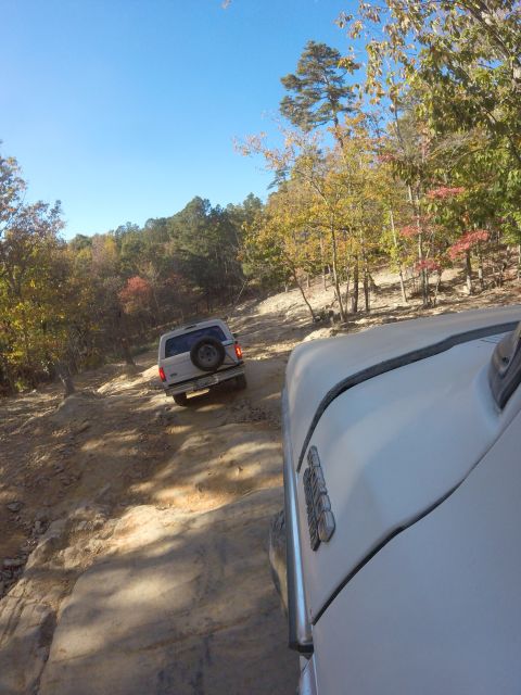 1979 Ford Bronco - A white Ford Bronco is driving up a rocky, dirt trail surrounded by trees with autumn foliage. Another white vehicle is in the foreground,…