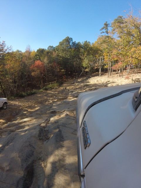 1979 Ford Bronco - A white vehicle, likely a 1979 Ford Bronco, navigates a rocky, off-road trail surrounded by autumn foliage. The side of the vehicle, showin…