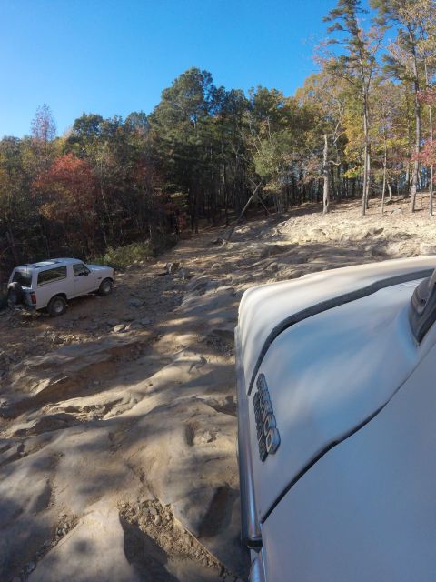 1979 Ford Bronco - A white Ford Bronco is parked on a rocky, off-road trail surrounded by trees with autumn foliage. Another white vehicle is partially visibl…