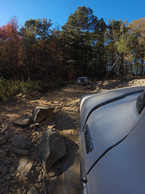 1979 Ford Bronco - A white Ford Bronco is seen from the perspective of another vehicle driving on a rocky, off-road trail surrounded by trees with autumn foli…