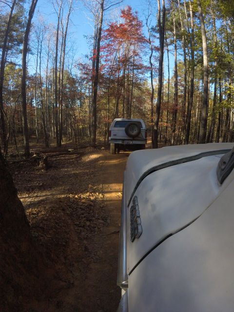 1979 Ford Bronco - Two SUVs navigate a dirt path through a forest during autumn.