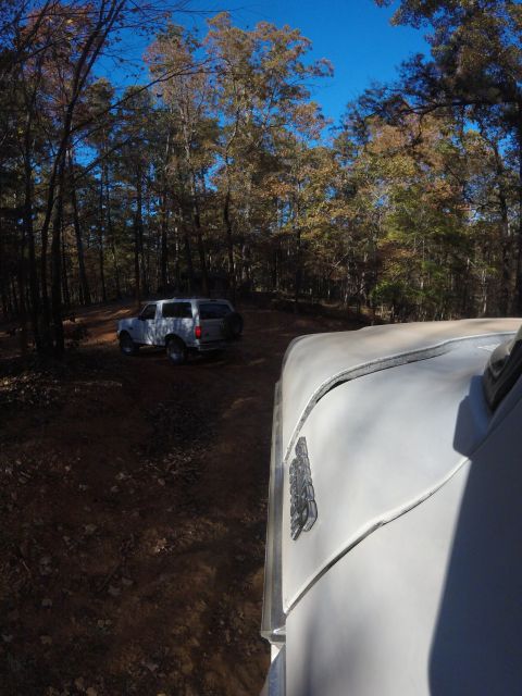 1979 Ford Bronco - Two SUVs navigate a wooded trail on a clear day, with autumn foliage visible in the trees.