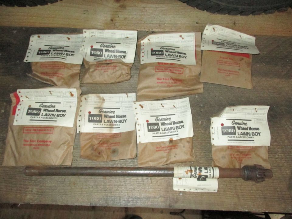 Several packages of Toro Wheel Horse Lawn-Boy parts and accessories, with a metal shaft in front