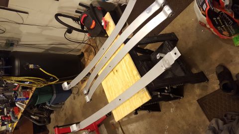 1994 Ford Bronco - Several leaf springs are arranged on a wooden surface, with various tools and equipment visible in the garage setting.
