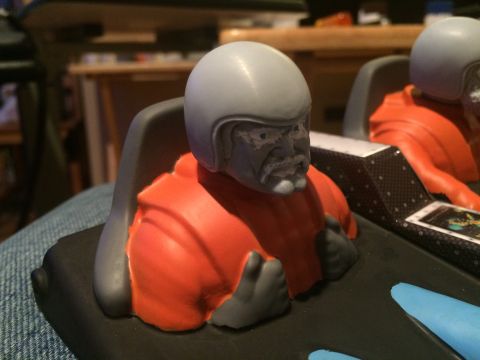 1989 Ford Bronco - Close-up of a model pilot figure wearing a gray helmet and orange flight suit, seated in a cockpit.