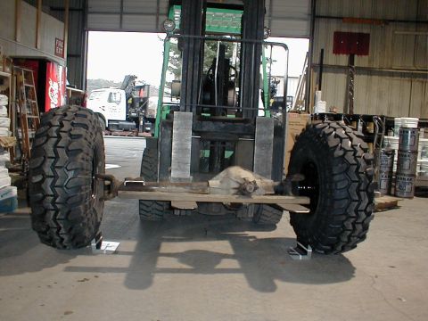1983 Ford Bronco - A rear axle assembly with oversized tires is being moved by a forklift in a workshop.