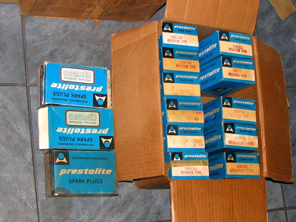 Stack of blue and white Prestolite spark plug boxes inside a cardboard box.