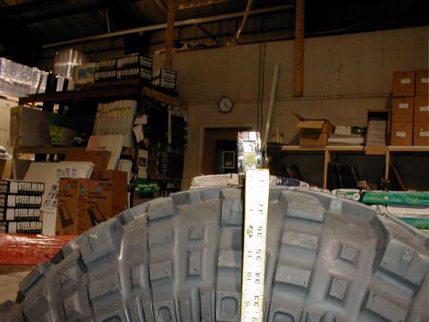 1983 Ford Bronco - Close-up of an oversized off-road tire with a chunky block tread pattern, standing upright with a yellow tape measure extended vertically u…