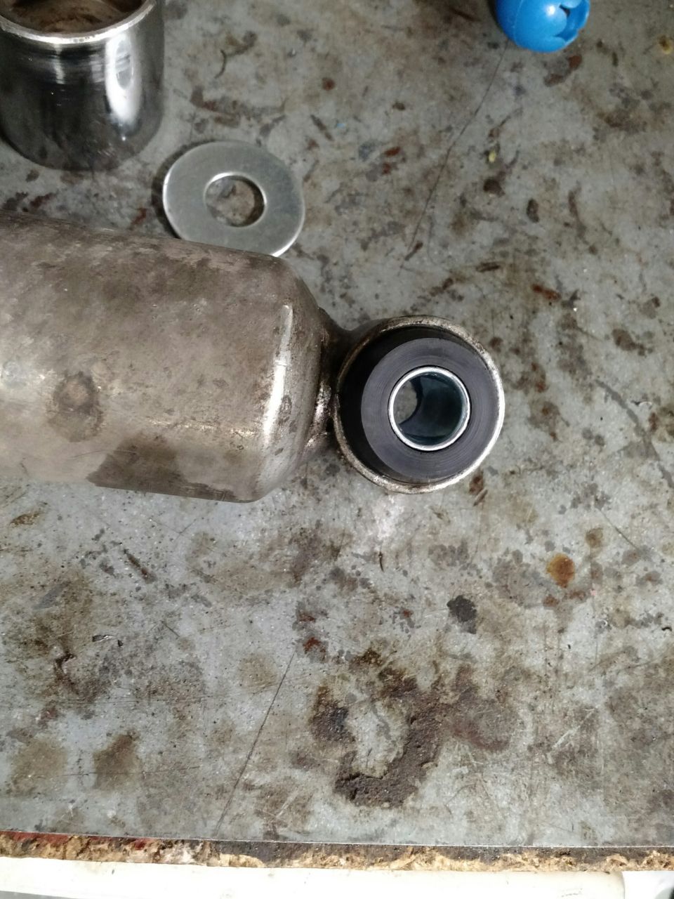 Shock absorber with bushing, washer, and metal cylinder on a dirty workbench