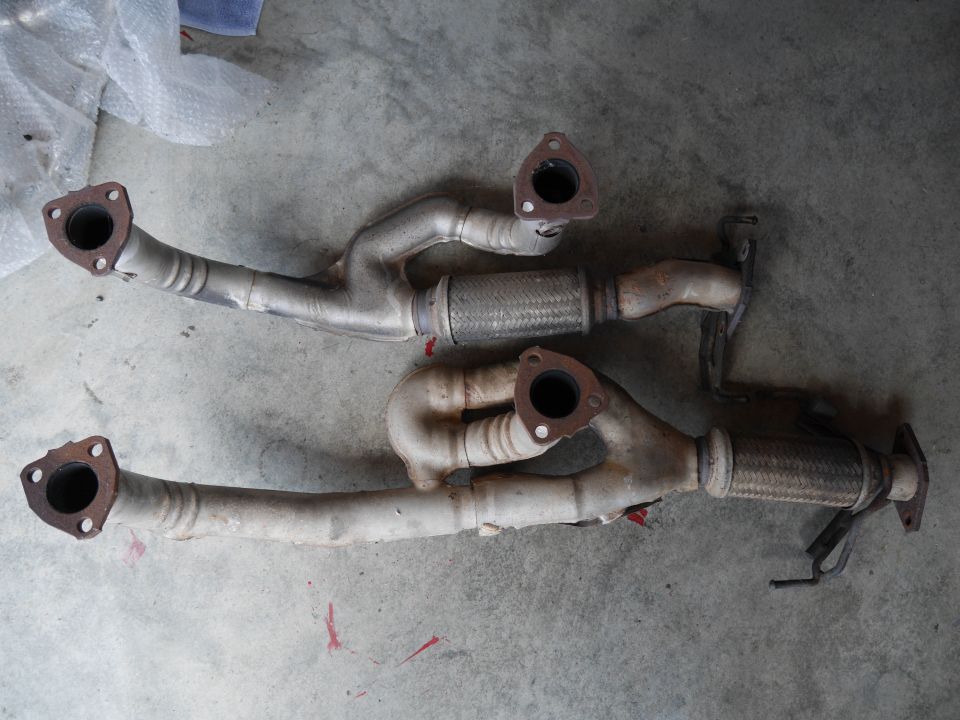 Two car exhaust systems with flexible pipes and flanges on a concrete floor.