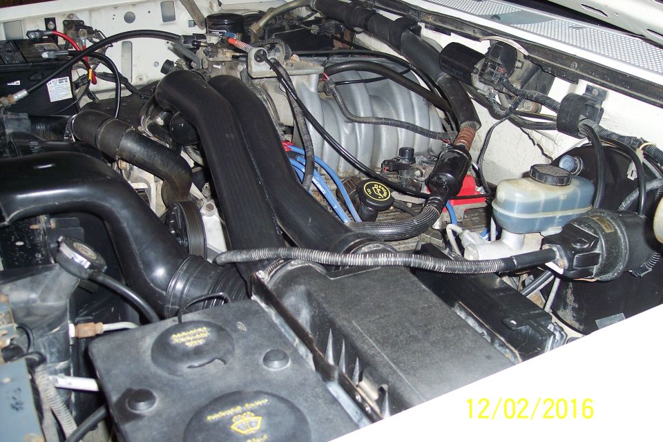 Engine bay of a 1990 Ford Bronco with hoses, battery, and brake fluid reservoir visible.