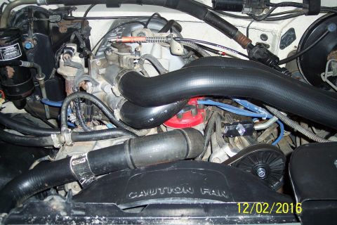 1990 Ford Bronco - Close-up view of an engine bay, prominent black hoses and a red distributor cap. The fan shroud has a 'CAUTION FAN' warning.