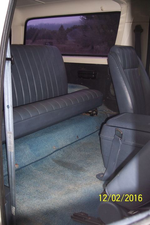 1990 Ford Bronco - The interior of a vintage SUV shows blue vinyl seats and blue carpet. The rear bench seat and a center console storage unit are visible, al…