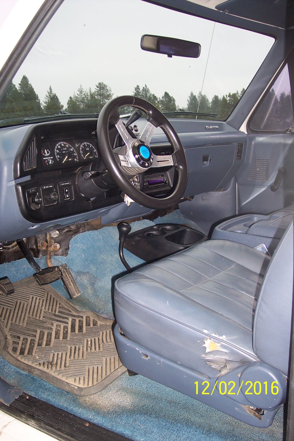 Interior of a vintage Ford Bronco showing dashboard, steering wheel, seats, and floor mat.