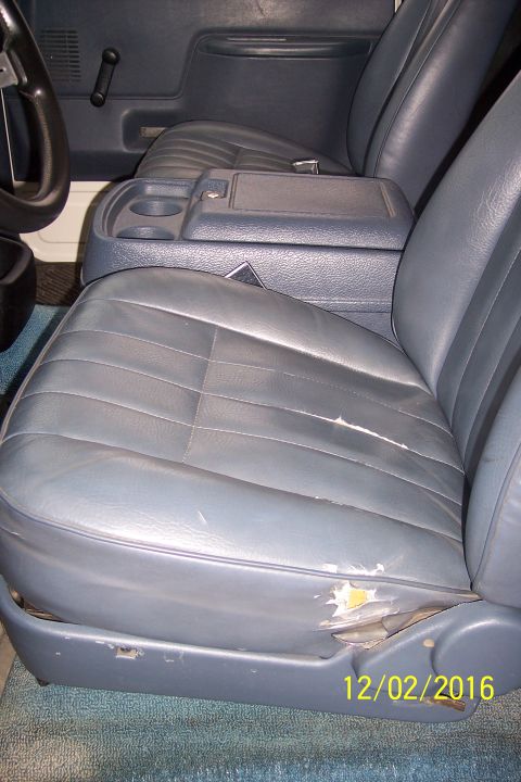 1990 Ford Bronco - The interior of a vintage Ford Bronco shows worn blue vinyl seats with visible damage on the driver's seat cushion. A center console with c…