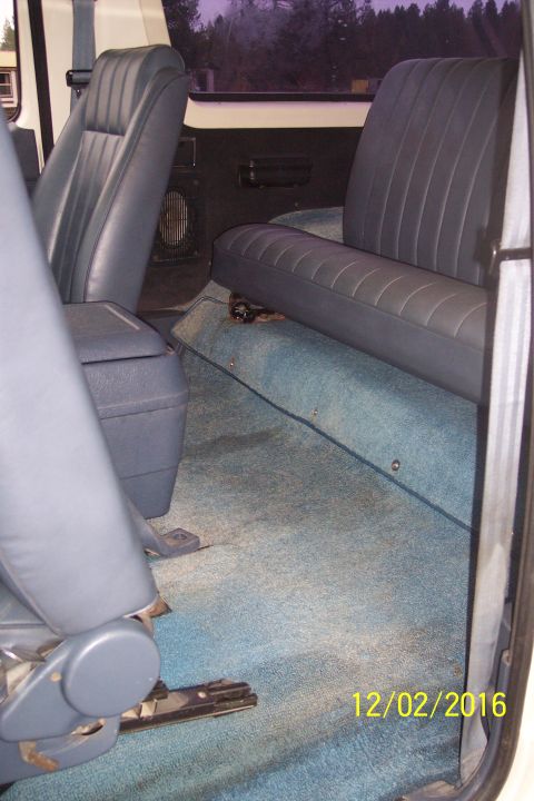1990 Ford Bronco - The interior of a vehicle shows blue carpeted flooring and dark blue vinyl seats, including a front bucket seat and a rear bench seat. A ce…