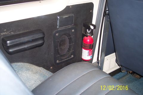 1990 Ford Bronco - Interior view of a vehicle showing a black door panel with a black armrest, a speaker grille, and a red fire extinguisher mounted on a blac…