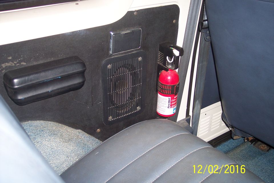 Interior of a vehicle showing a black door panel with a fire extinguisher and speaker grille.