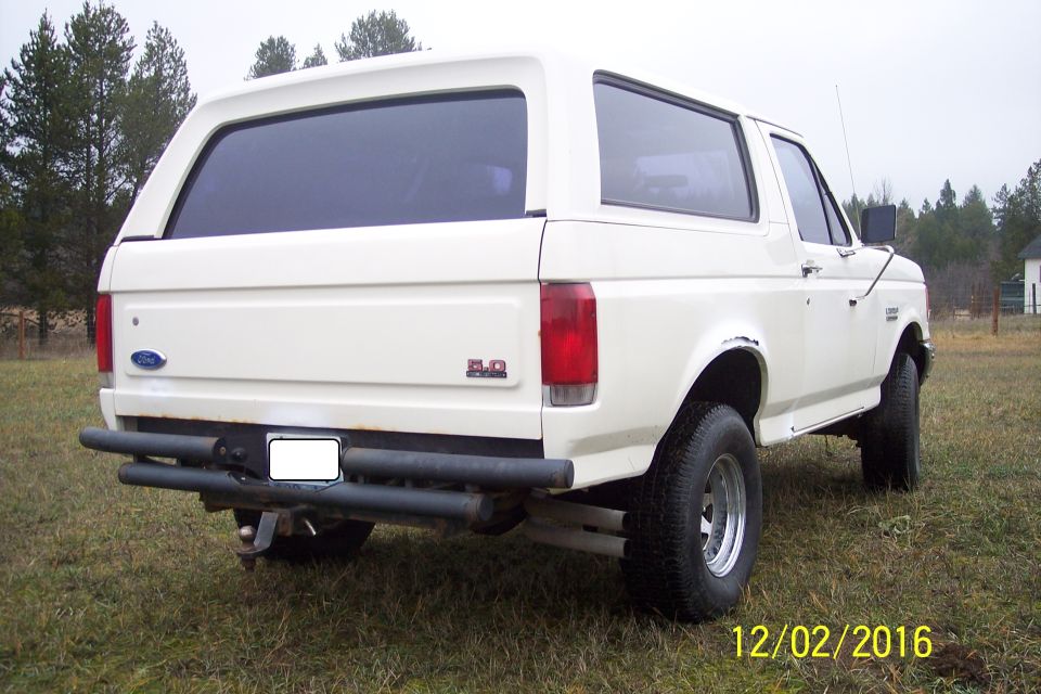 White 1990 Ford Bronco rear 3/4 view with custom bumper and tinted windows.
