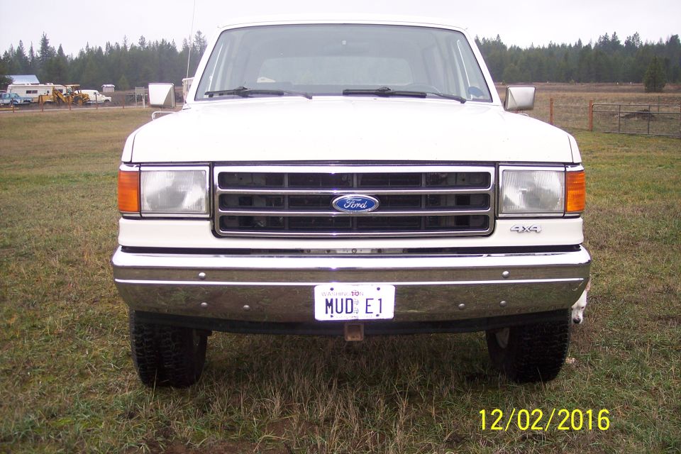 1990 Ford Bronco front view, white, with custom license plate "MUD E1" and "4X4" badging.