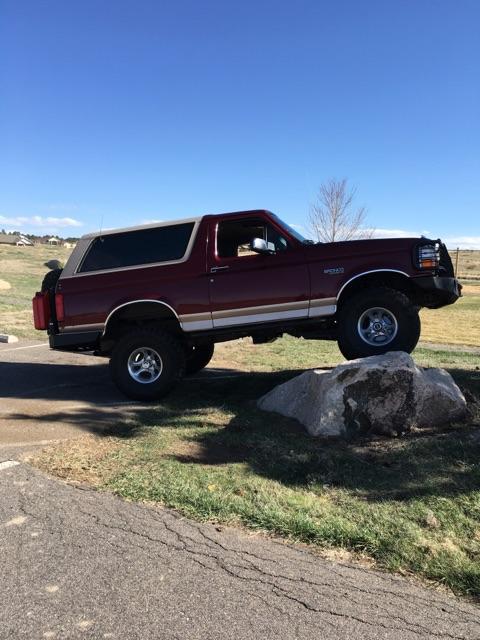 1996 Ford Bronco - A red 1996 Ford Bronco is parked on a grassy area with a large rock in front of its tires. The vehicle is viewed from the side against a cl…
