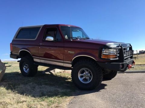 1996 Ford Bronco - A maroon Ford Bronco is parked on a grassy area with a clear blue sky in the background. The vehicle has a lifted suspension and a custom f…