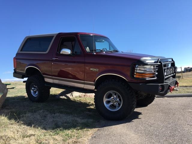 Maroon Ford Bronco with lifted suspension and custom front bumper parked outdoors.