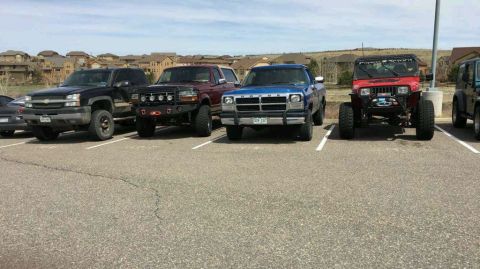 1996 Ford Bronco - A row of modified trucks and Jeeps are parked in a lot with houses in the background. The vehicles include a black Chevrolet Silverado, a r…