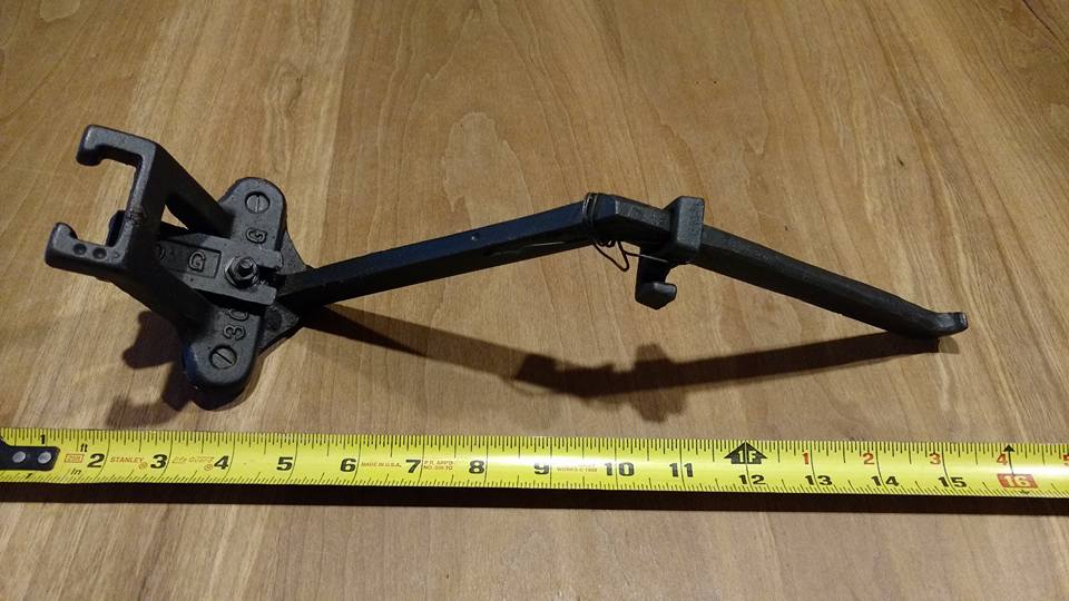 Black metal automotive tool with jaws and handle on a wooden surface with a measuring tape.