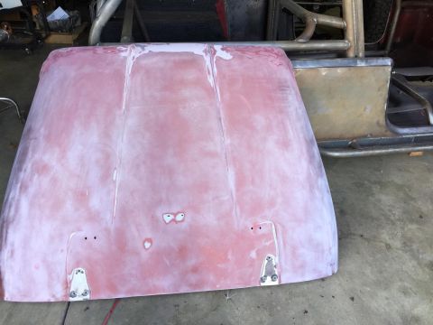 1985 Jeep CJ7 - A red vehicle hood is shown from a top-down perspective, resting on a concrete floor. The hood appears to be prepped for painting with a pr…