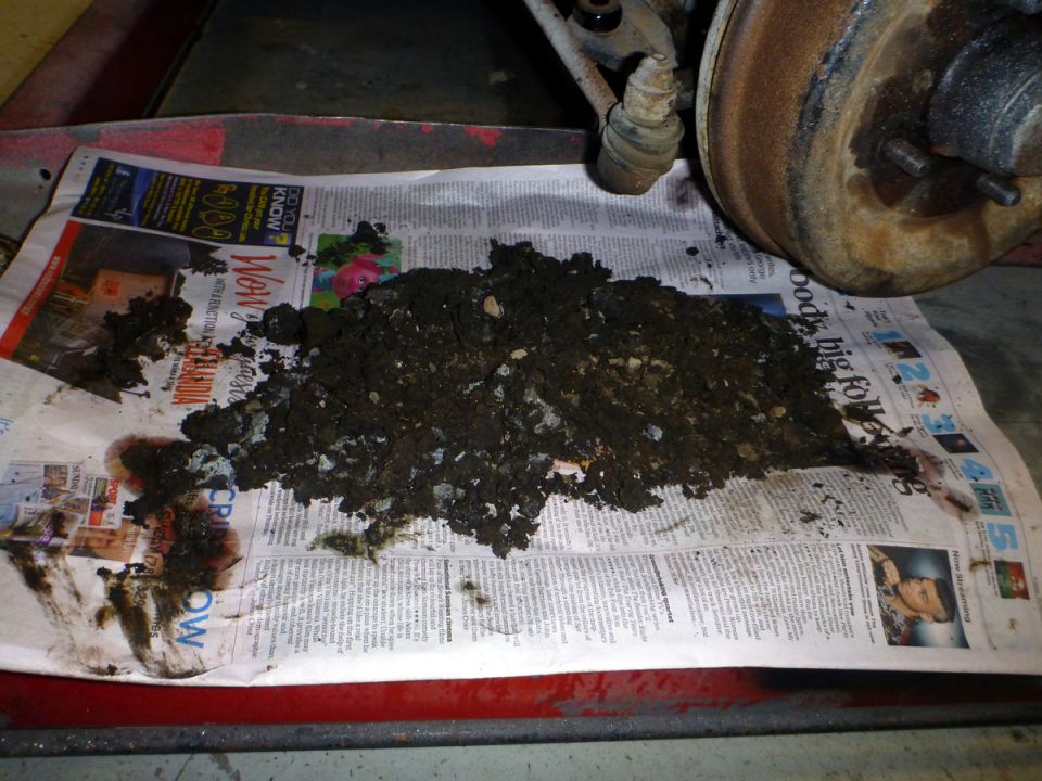 Pile of brake dust and debris next to a rusty brake drum and suspension parts.