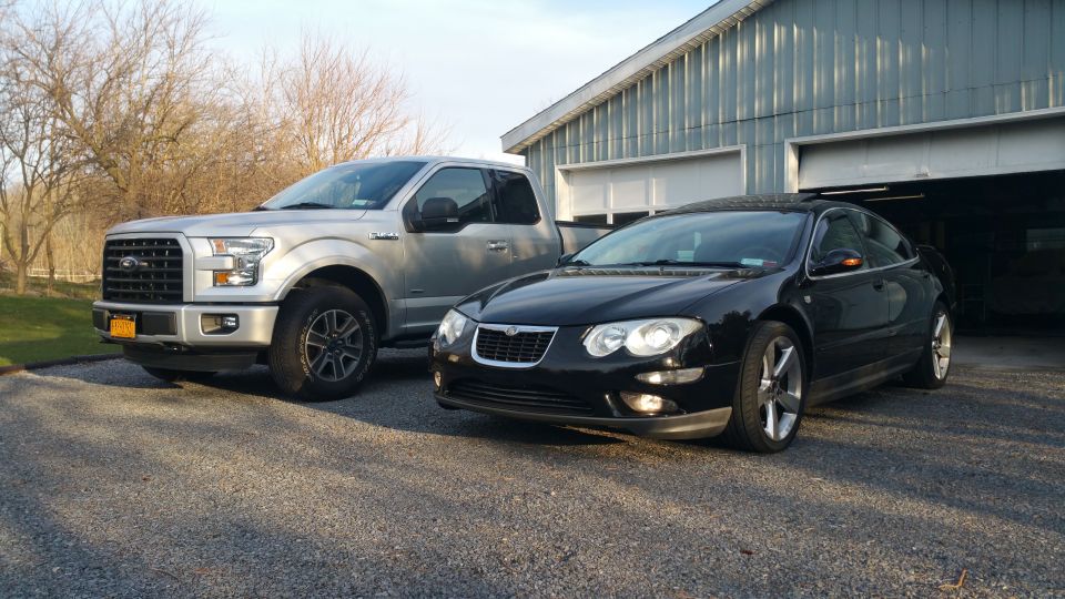 Silver Ford F-150 pickup truck and black Chrysler sedan parked in front of a garage.