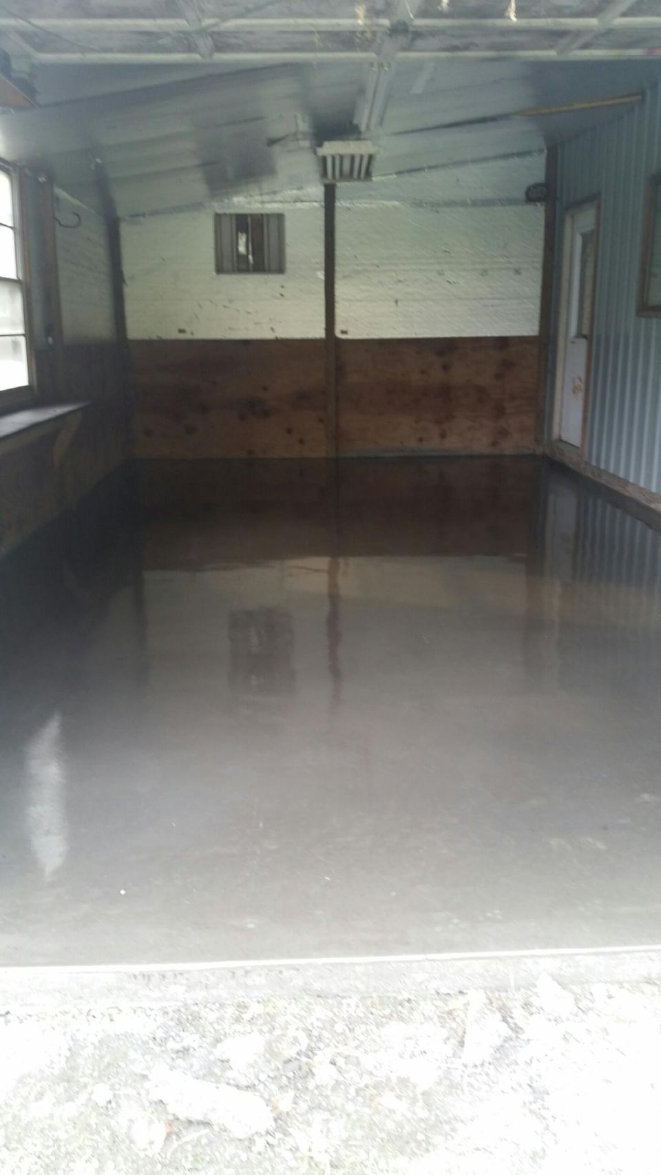 Interior of a structure with a new concrete floor, wood and metal walls, window, and door.